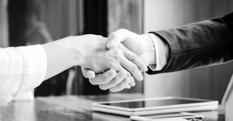 Two professionals shaking hands across a meeting table after agreeing terms.