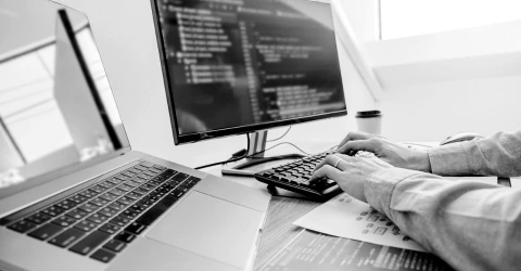 A developer writing code at a workstation with a laptop and a monitor full of source code.